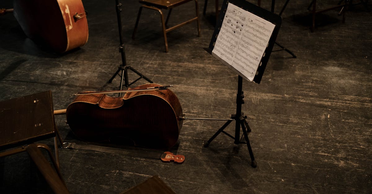 A cello rests on an empty stage with a music stand and scattered chairs, evoking classical music ambiance.