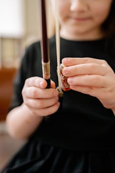 A child is applying rosin to a cello bow in a close-up shot, highlighting musical preparation.