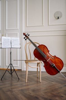 A cello resting against a chair beside a music stand in a classic room setting.